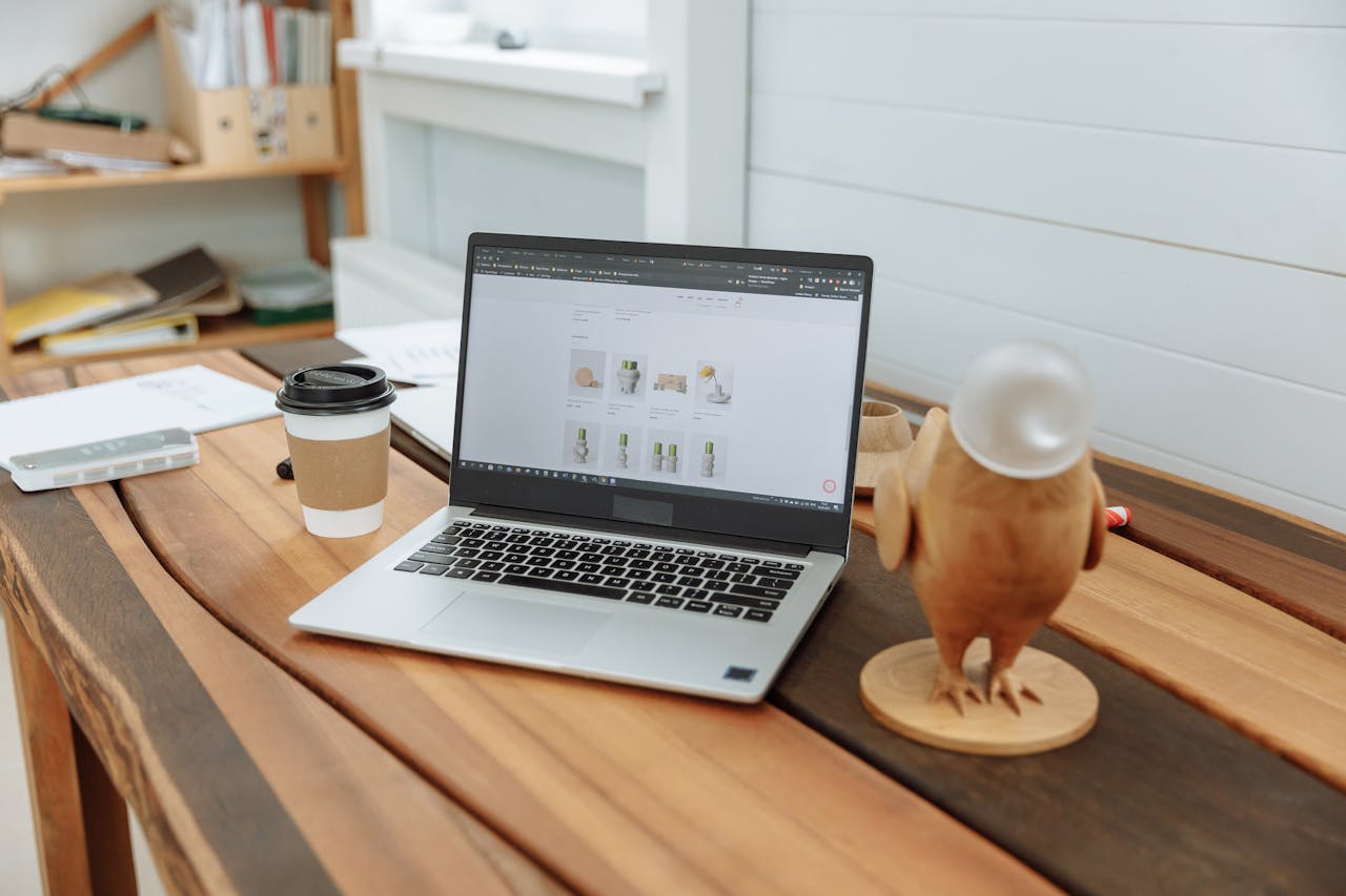 hero-img-02 A contemporary office desk setup featuring a laptop, coffee cup, and wooden figurine on a wooden table.